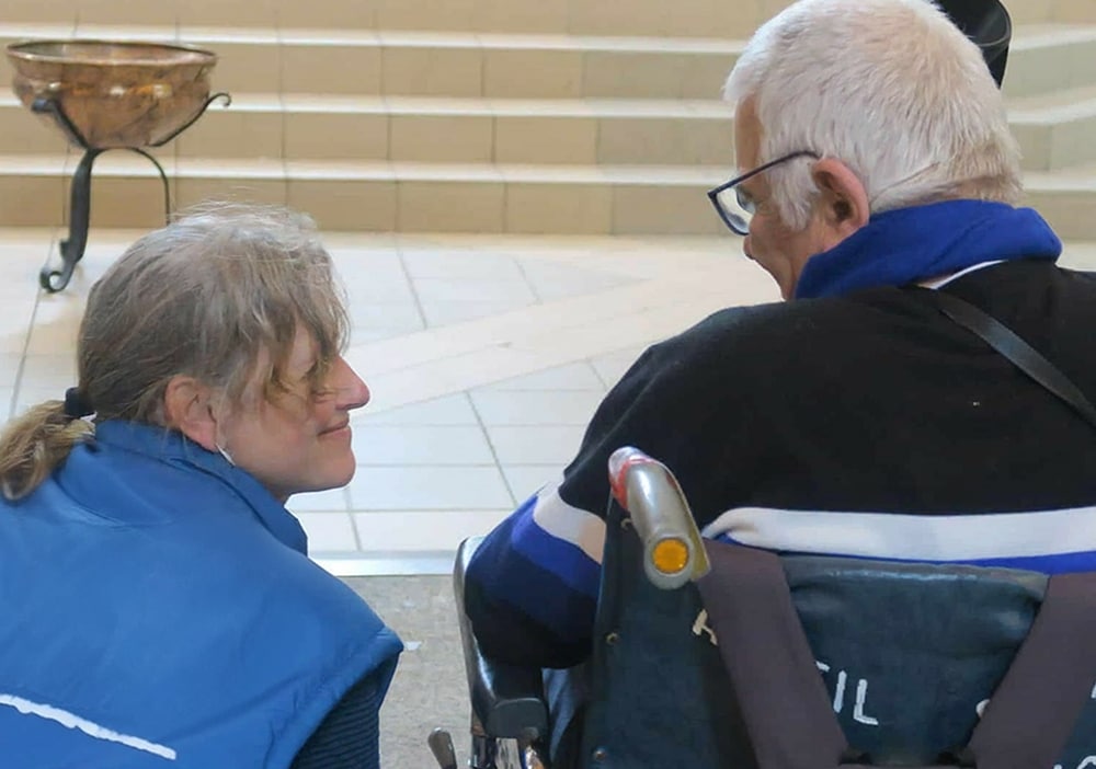 accompagner les plus démunis une dame porte assistance a une personne âgée en fauteuil roulant